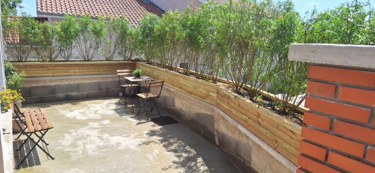 Terrasse protégée des regards par une jardinière en bois plantée, avec arrosage goutte-à-goutte