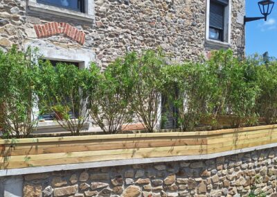 Jardinière en bois plantée en brise-vue sur un muret en pierre, devant une maison de village à Fontanès
