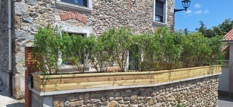 Jardinière en bois plantée en brise-vue sur un muret en pierre, devant une maison de village à Fontanès